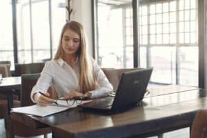 Business woman sitting at desk with laptop and writing on notepad