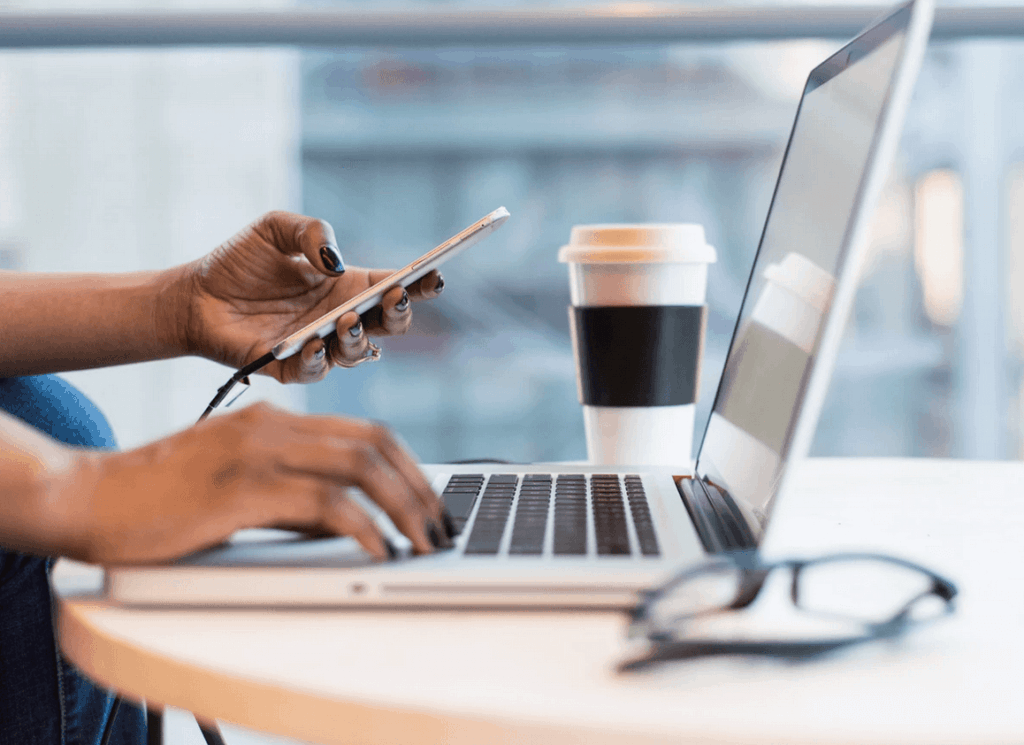Woman using cellphone and laptop at desk