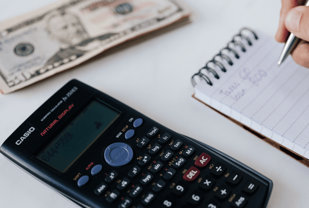 Desk with calculator and US dollars and person writing on notepad