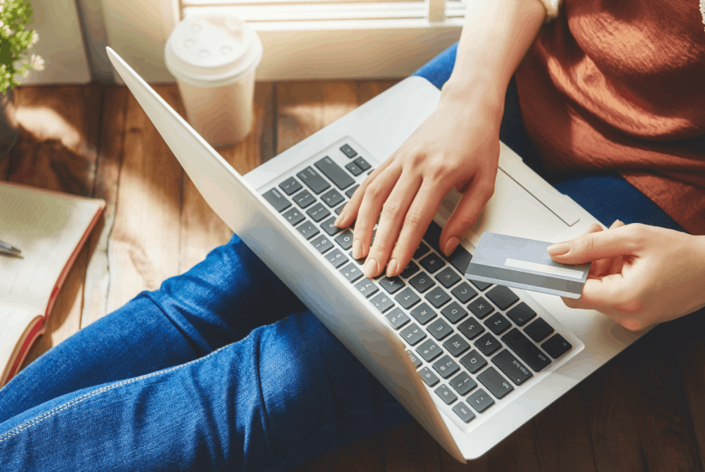 Woman sitting on floor using credit card to purchase something on laptop