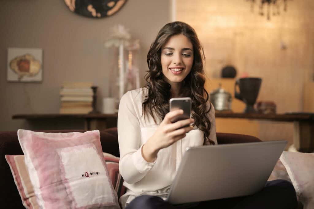woman sitting on couch with laptop, using cellphone
