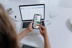 Person sitting at desk with laptop on it using cellphone to visit website