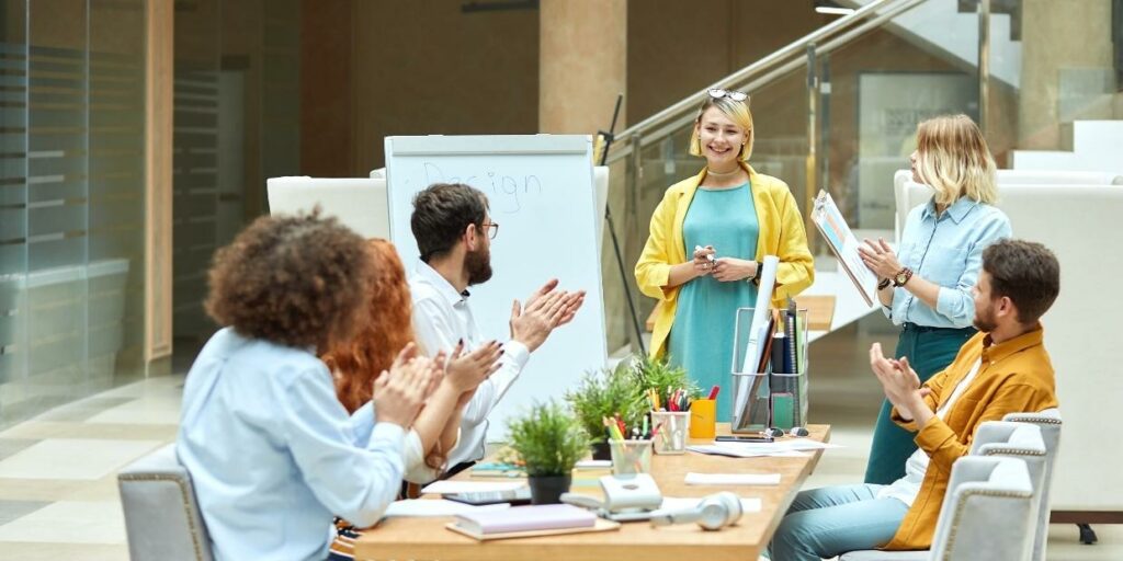 Colleagues sitting at a table in a design meeting applauding a co-worker