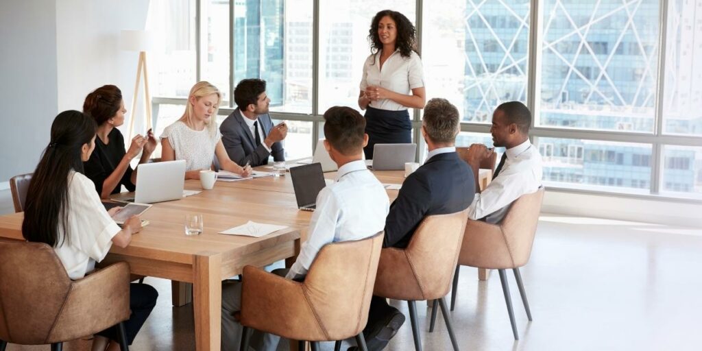 A work meeting with a woman talking to co-workers sat at a table