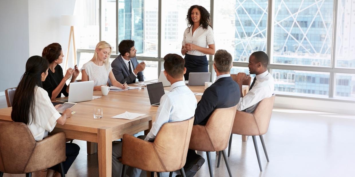 A work meeting with a woman talking to co-workers sat at a table