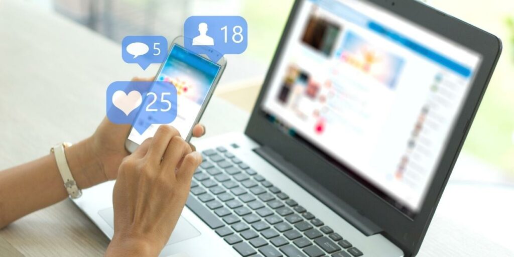 A laptop next to a person on their cellphone with social media icons